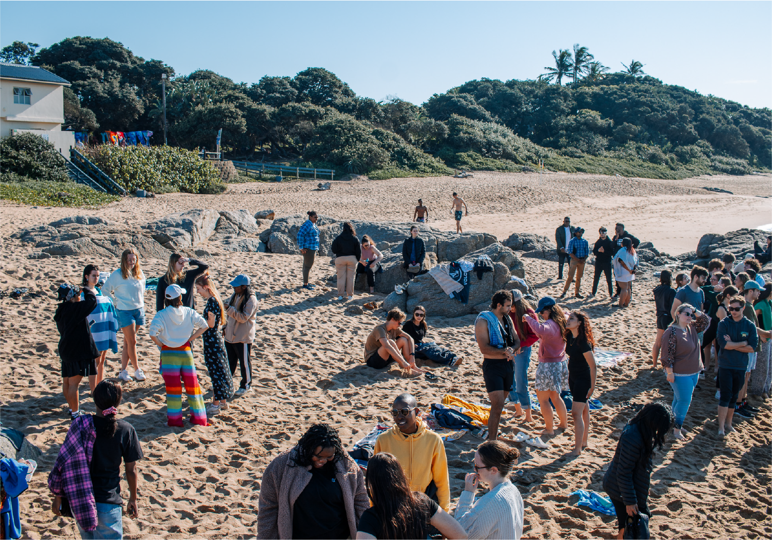 Group of campers enjoying a sunny morning on the beach near Camp Anerley, socialising and relaxing by the ocean.