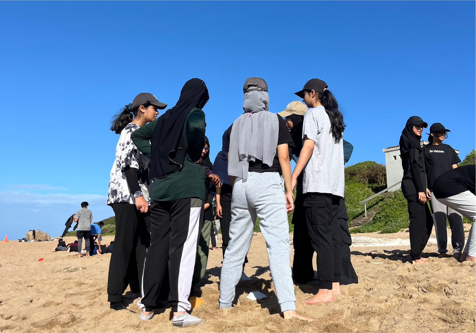 Campers gathered on the beach during a group challenge near Camp Anerley under clear blue skies.