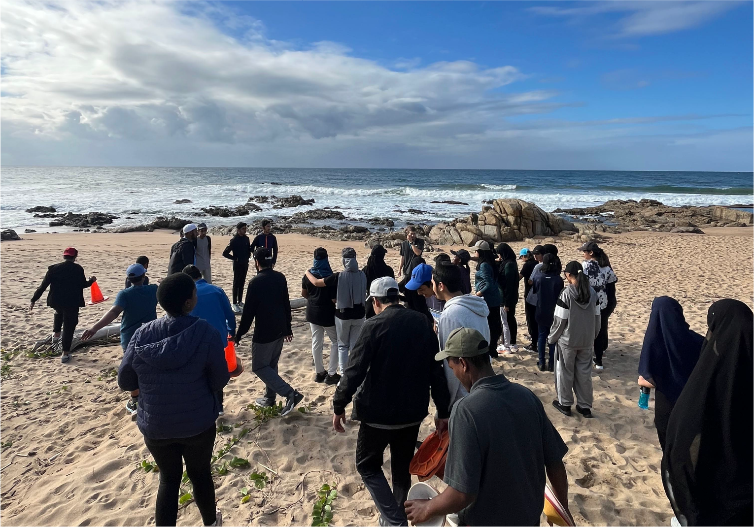 Group of campers participating in a team activity on the beach near Camp Anerley under a bright blue sky.
