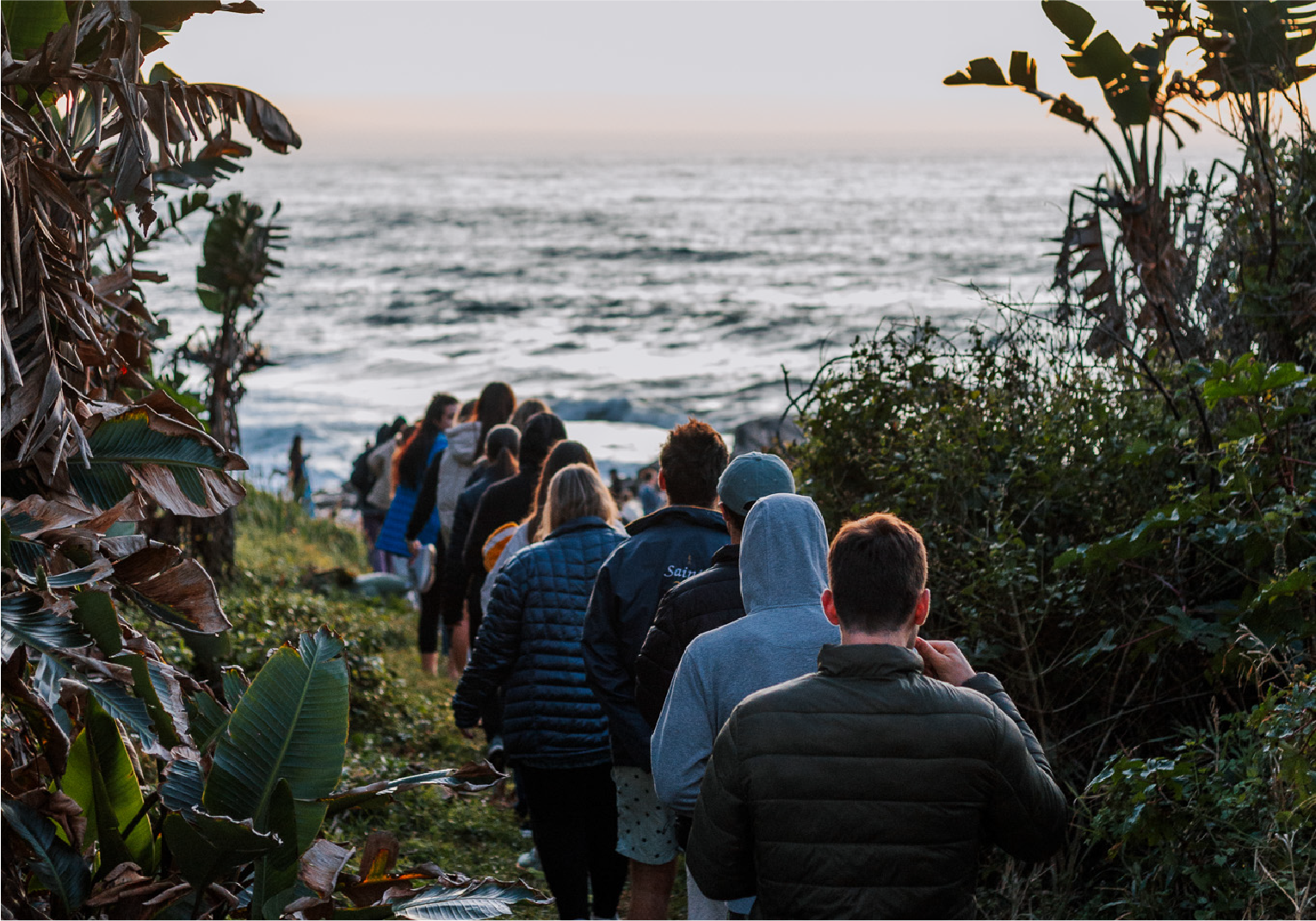 Group of campers walking down a coastal path toward the beach at sunrise near Camp Anerley.