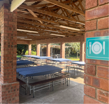 Open-air dining area at Camp Anerley with blue tablecloths, benches, and a brick pavilion structure.