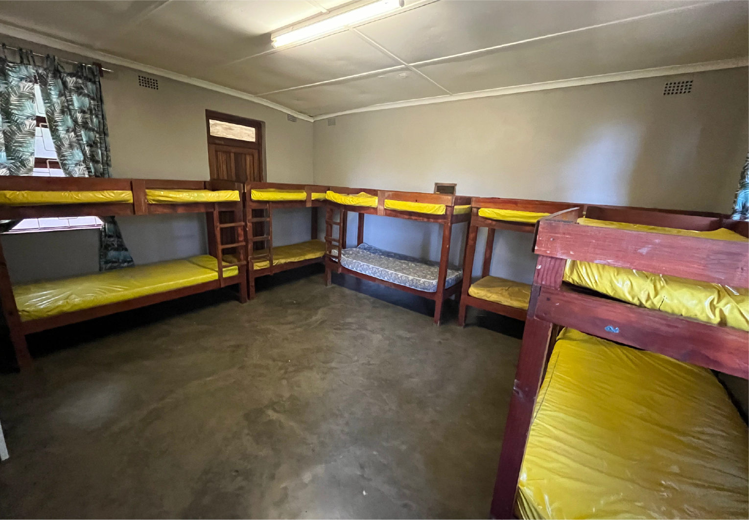 Bunk-bed dormitory at Camp Anerley with yellow mattresses, wooden frames, and bright natural light through curtained windows.