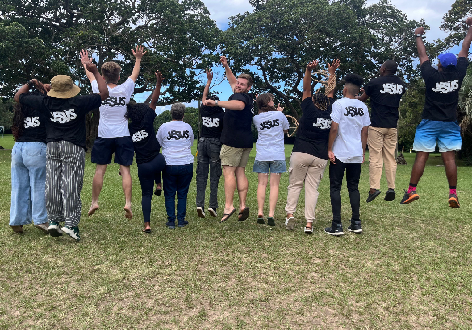 Group of campers jumping with joy outdoors at Camp Anerley, wearing matching shirts that celebrate unity and faith.