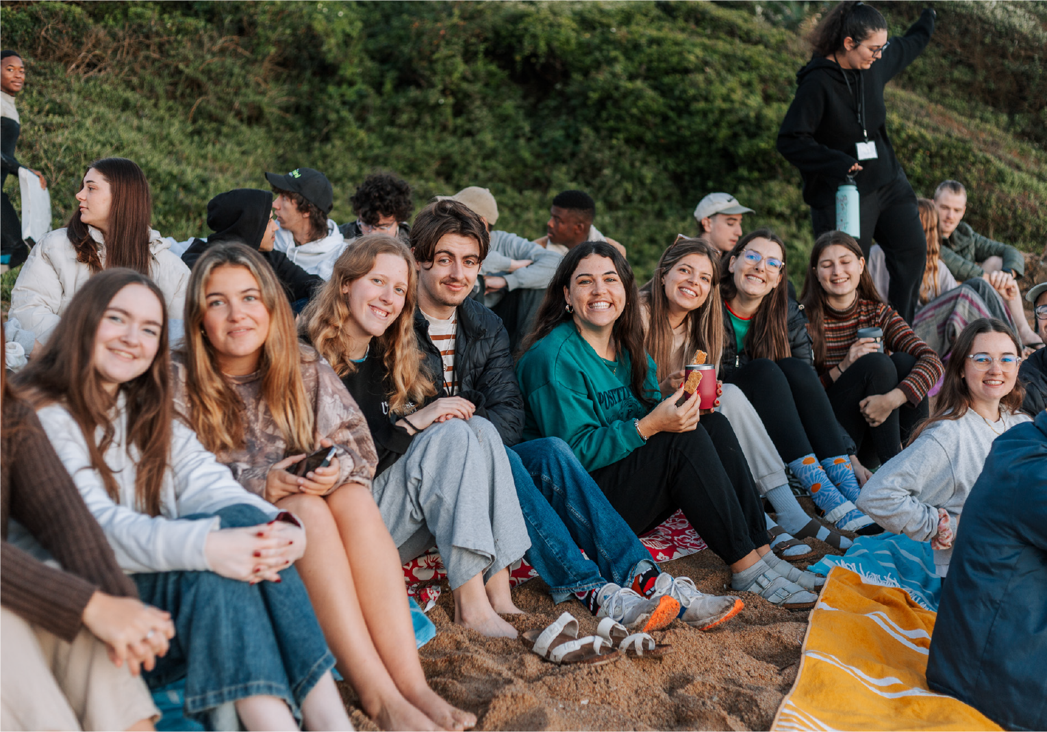 Group of smiling young people sitting together outdoors, enjoying a relaxed moment at Camp Anerley.