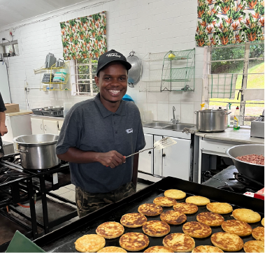 Camp Anerley kitchen team member smiling while cooking golden patties on a griddle.