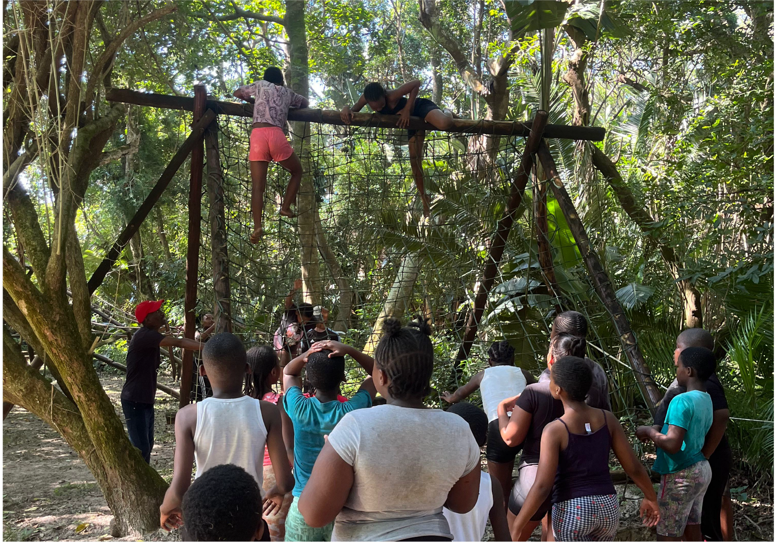 Children at Camp Anerley climbing a rope obstacle in the forest with group support and encouragement.