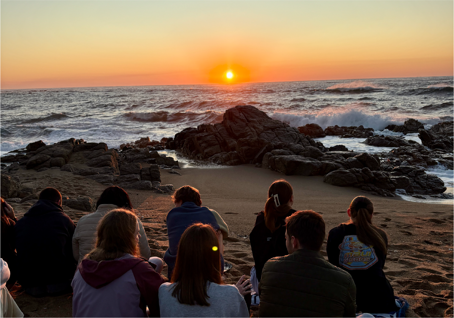 Campers sitting together on the beach at sunrise near Camp Anerley, watching the sun rise over the ocean.