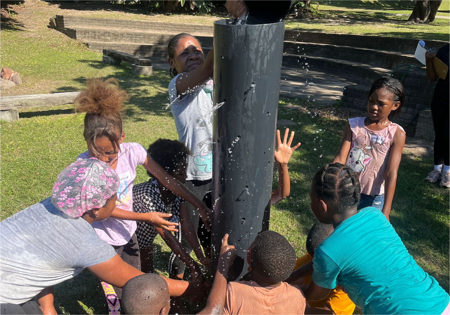 Children working together in a fun water challenge at Camp Anerley, filling a tall pipe as water splashes around.