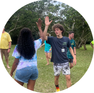 Two campers high-fiving during an outdoor activity at Camp Anerley, surrounded by trees and open space.