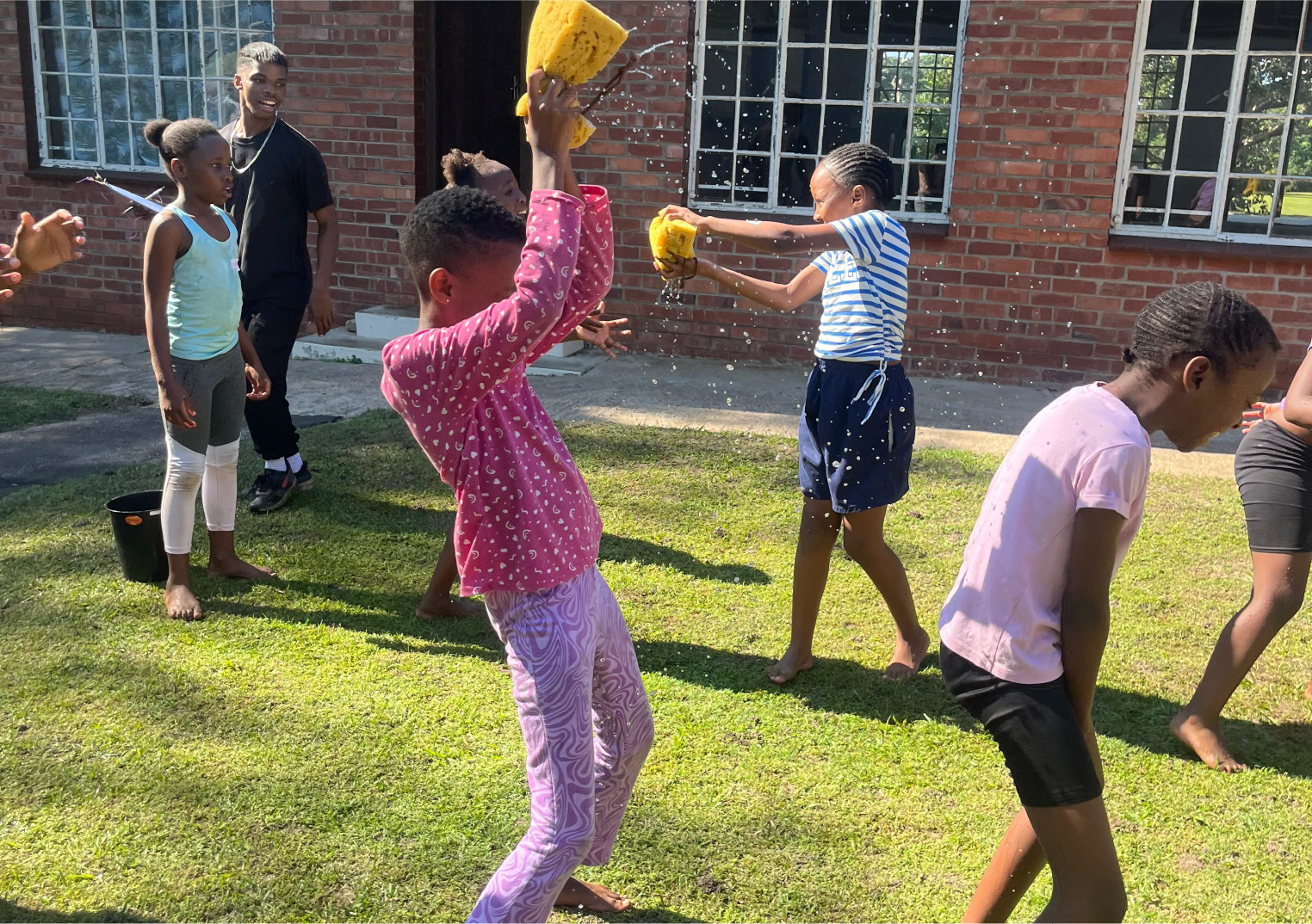 Children at Camp Anerley playing a fun outdoor water game with large sponges on a sunny day.